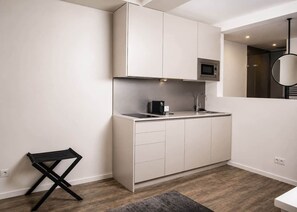 A modern kitchen with white cabinetry, a black countertop, and a small black stool. - The Faces | Premium Studio | Balcony | 201 (Berlin)