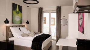 A modern bedroom with a bed, bedside tables, a desk, and artwork on the walls. - The Faces | Premium Studio | Balcony | 201 (Berlin)