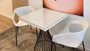 A modern interior with a white table and two white chairs, a textured wall, and a large painting of lips with stars. - The Faces | Premium Studio | Balcony | 203 (Berlin)