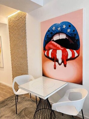 A modern interior with a white table and two white chairs, a textured wall, and a large painting of lips with stars. - The Faces | Premium Studio | Balcony | 203 (Berlin)