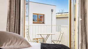 A bedroom with a bed, a small table, and chairs, a balcony with a view of a building, and a window with curtains. - The Faces | Premium Studio | Balcony | 203 (Berlin)