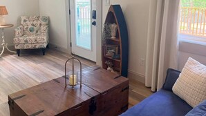 Een woonkamer met een blauwe bank, een houten kist, een decoratieve stoel en uitzicht door een deur.