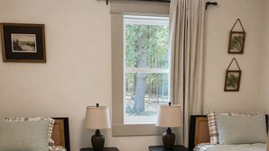 Een slaapkamer met twee bedden, een raam met uitzicht op bomen, een vloerkleed en twee nachtkastjes met lampen.