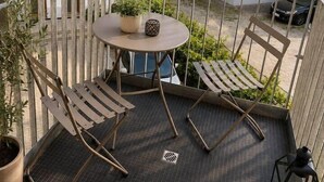 Ein Balkon mit rundem Tisch, zwei Stühlen, einem Blumentopf und einer Laterne.