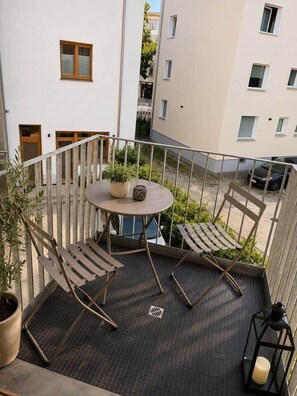 Ein Balkon mit rundem Tisch, zwei Stühlen, einem Blumentopf und einer Laterne.