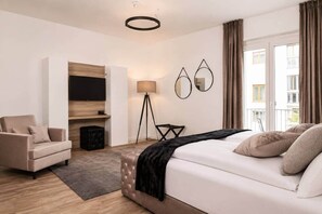 A modern hotel room with a bed, a sofa, a desk, and a large window. - The Faces | Suite | Balcony | 001 (Berlin)