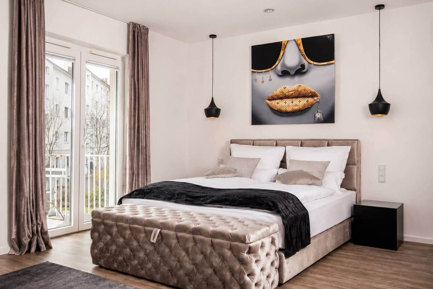 A bedroom with a bed, bedside tables, a large window, and a view of buildings outside.
