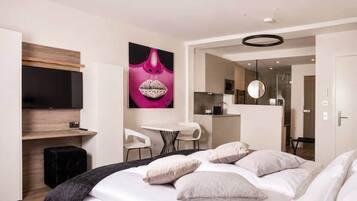 Ein modernes Hotelzimmer mit Bett, Schreibtisch, Stuhl, Fernseher und einem durchgegangene Tür sichtbaren Badezimmer.