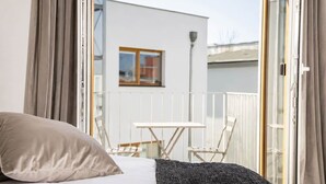 A bedroom with a bed, a window, and a balcony with a table and chairs. - The Faces | Premium Studio | Balcony | 204 (Berlin)