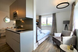 A compact hotel room with a kitchenette, a bed, a seating area, and a view of the outdoors. - The Faces | Premium Studio | 207 (Berlin)
