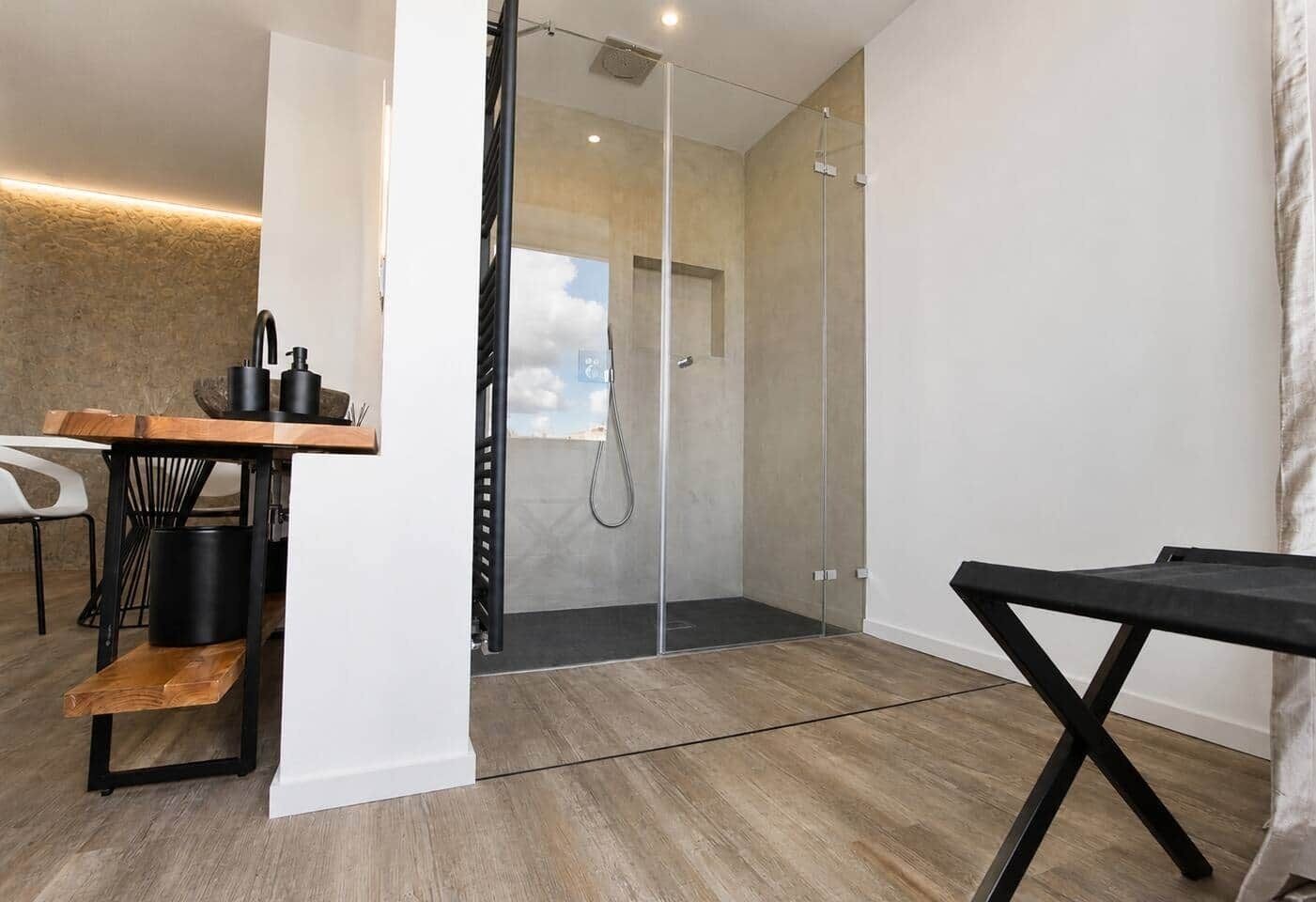 A modern bathroom with a glass shower enclosure, a wooden bench, and a small table with a black surface.