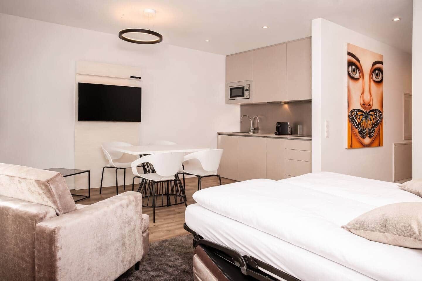 A modern hotel room with a bed, a desk, a chair, a flat-screen TV, a microwave, and a painting on the wall.
