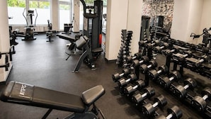 Et fitnesscenter med forskellig træningsudstyr, herunder løbebånd, styrkemaskiner og en bænk.
