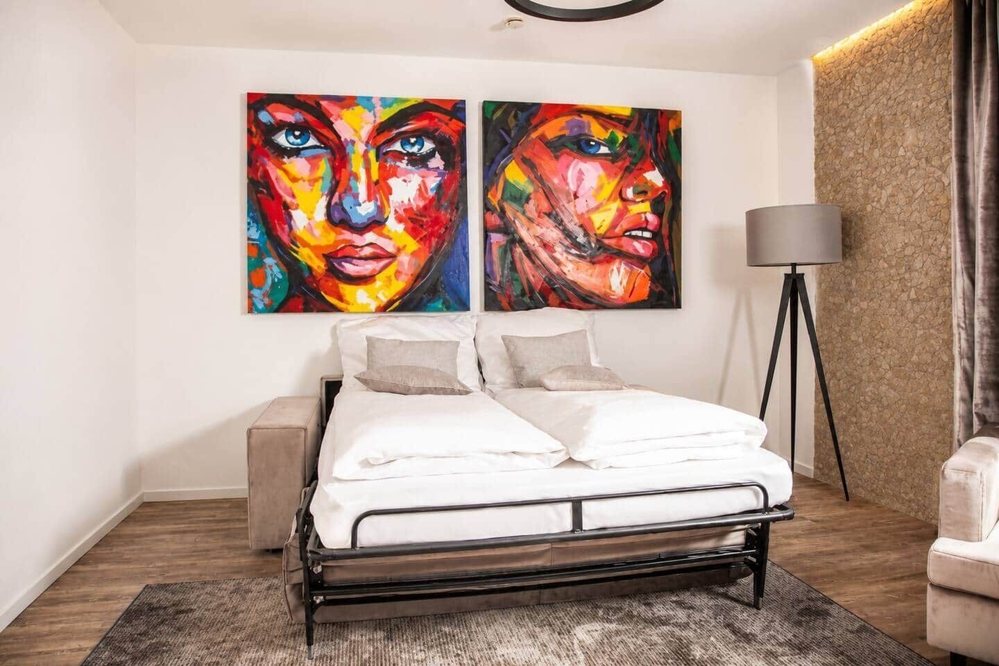 Un dormitorio moderno con una cama, dos cuadros, una lámpara y una pared con textura de piedra.