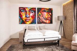 Ein modernes Schlafzimmer mit einem Bett, zwei Bildern, einer Lampe und einer Wand mit Steinoptik.