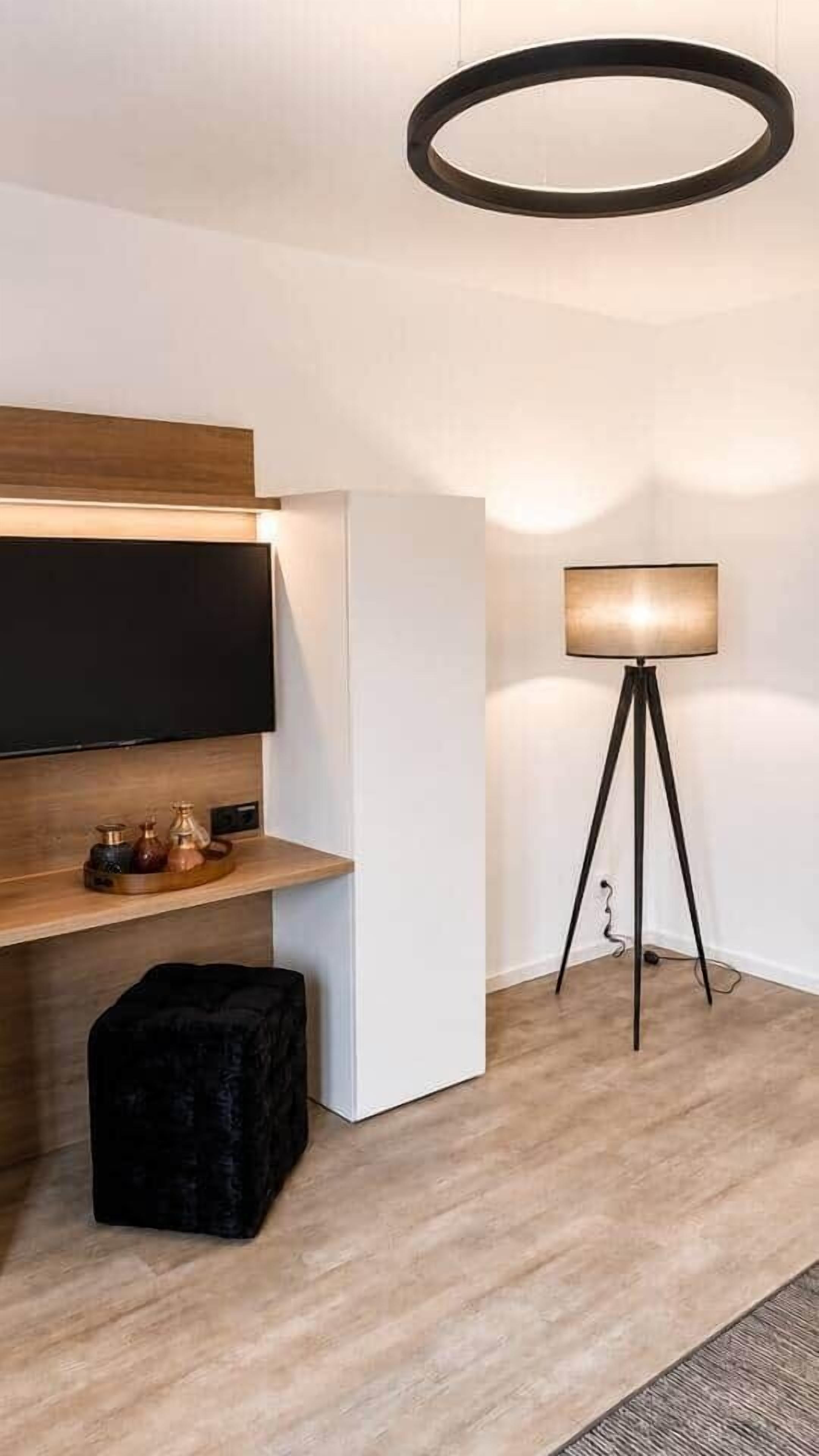 A modern interior with a flat-screen TV mounted on a wooden shelf, a floor lamp, and a black ottoman.