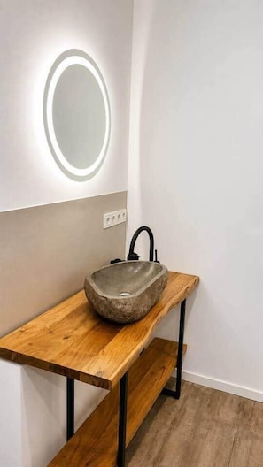 Ein Badezimmer mit einem Holzkosmetikschrank, einem Steinsinkens und einem runden Spiegel mit Beleuchtung.