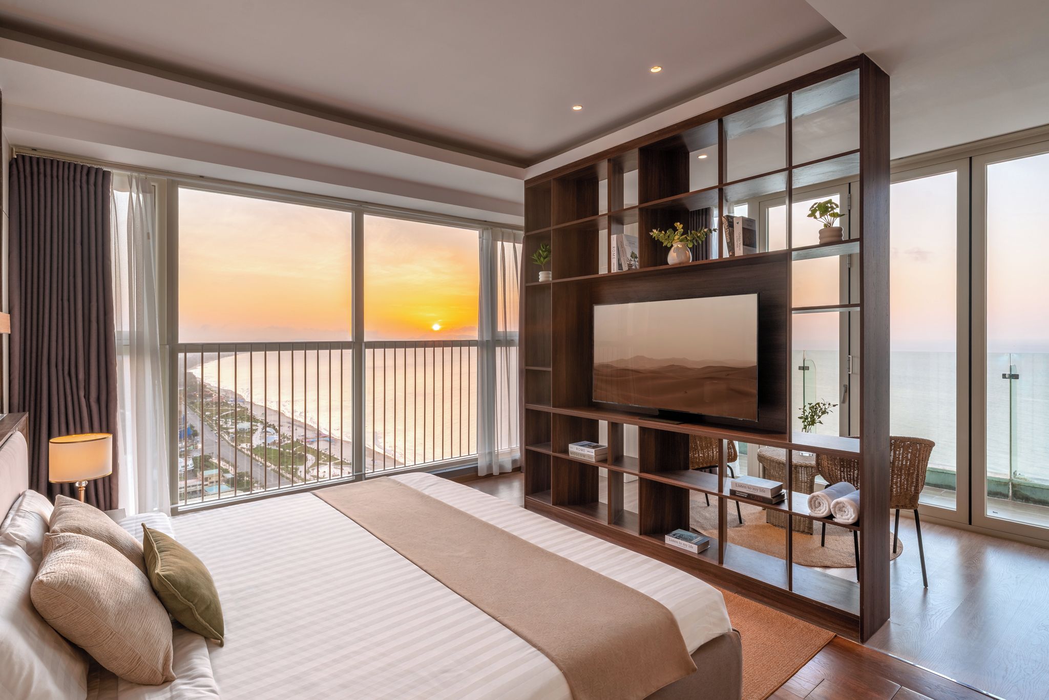 Une chambre d’hôtel moderne dotée d’un grand lit, d’une télévision, d’un balcon offrant une vue sur le coucher de soleil et d’un coin repas.