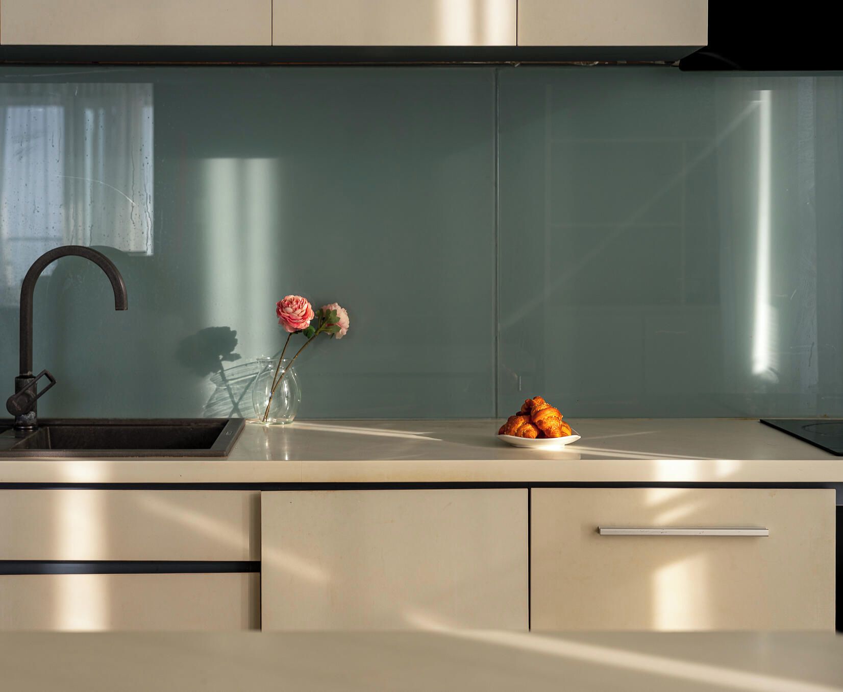 A modern kitchen with a stainless steel sink, a vase with flowers, and a plate of food.