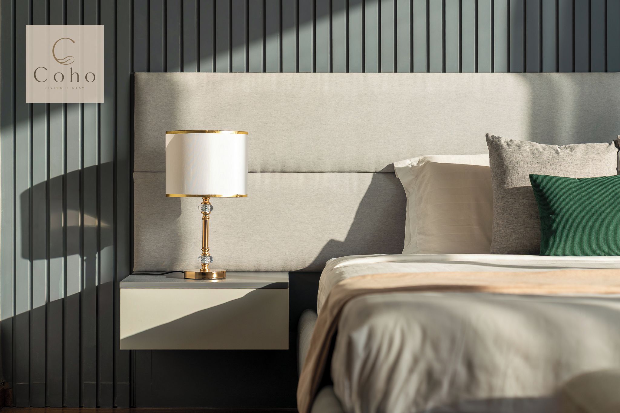A neatly made bed with a headboard, a bedside lamp, and a pillow on a nightstand.