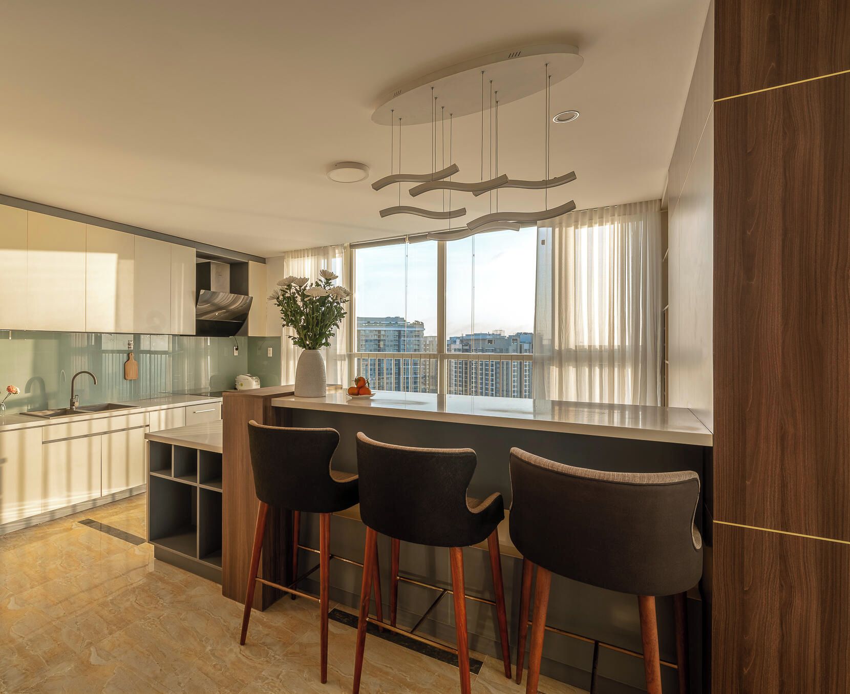 A modern kitchen with a bar area, large windows, and a city view.