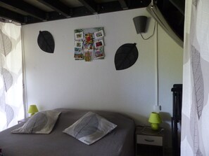 Ein Schlafzimmer mit einem Bett, zwei Kissen, einem Nachttisch, einer Lampe und einer Wand mit Fotos und blattförmigen Verzierungen.