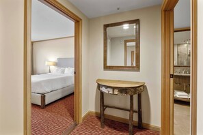 Habitación de hotel con cama, mesita de noche, espejo y baño visible a través de una puerta abierta.