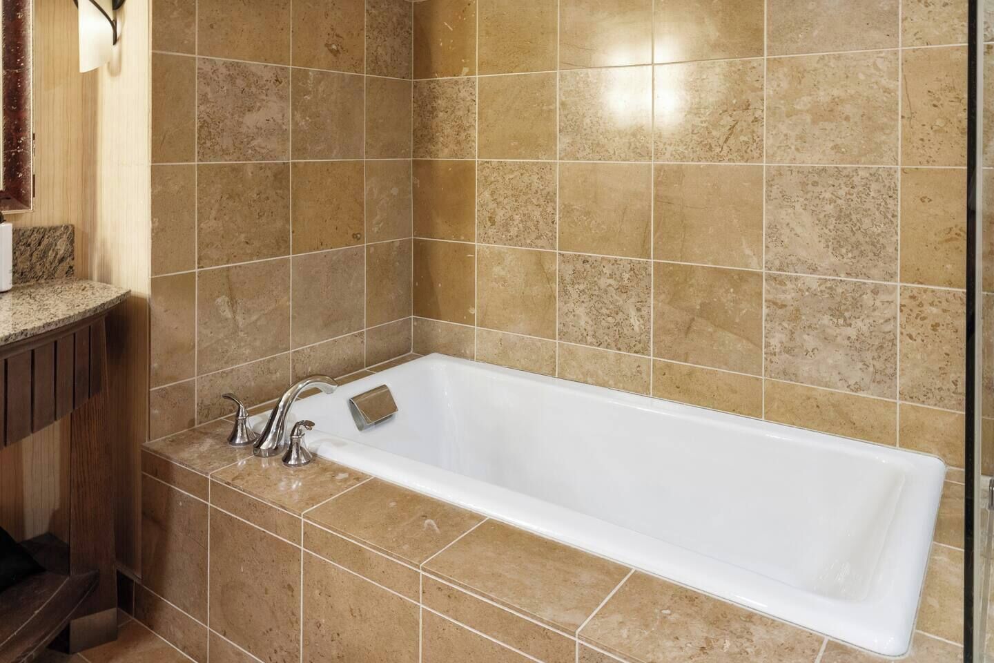 Un baño con una bañera blanca, un tocador de madera y paredes cubiertas de baldosas color crema.