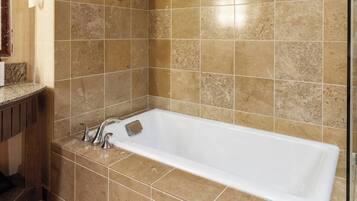 Un baño con una bañera blanca, un tocador de madera y paredes cubiertas de baldosas color crema.