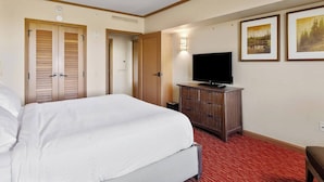 A hotel room with a bed, a television, a dresser, and two doors.