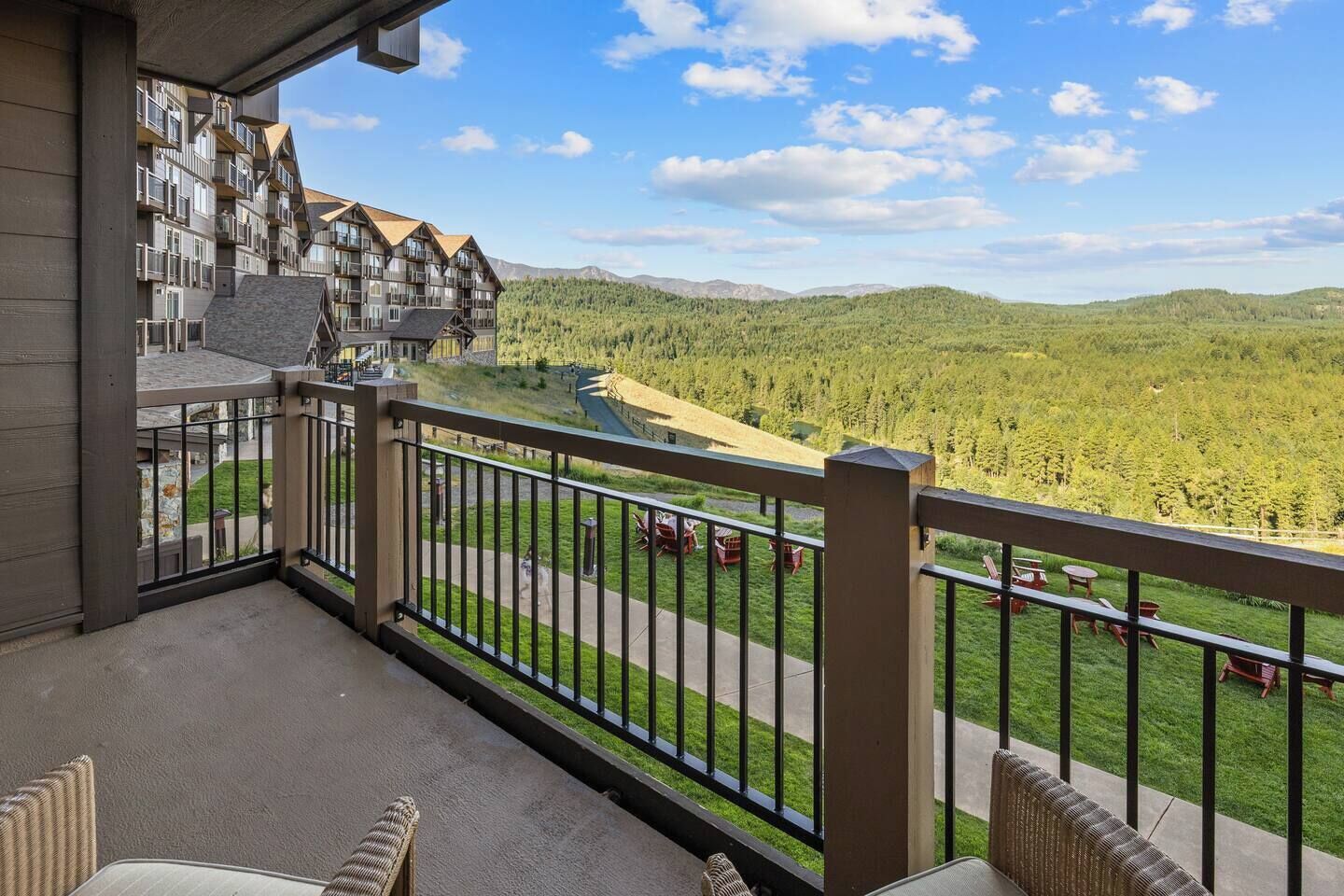 A balcony with a view of a mountainous landscape, a building with multiple balconies, and outdoor seating.