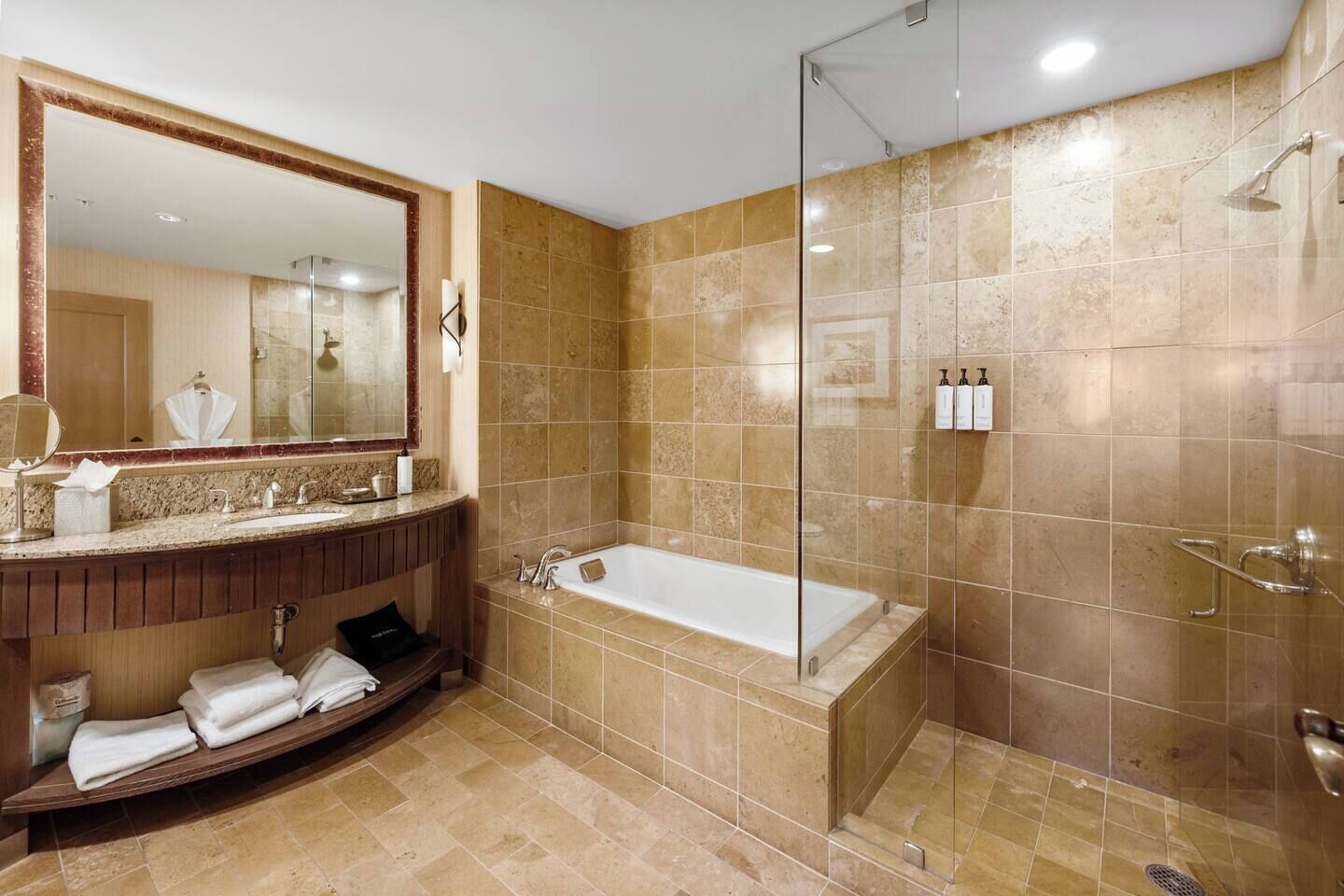 Un baño moderno con bañera, cabina de ducha con mampara de vidrio y tocador con espejo y toallero.