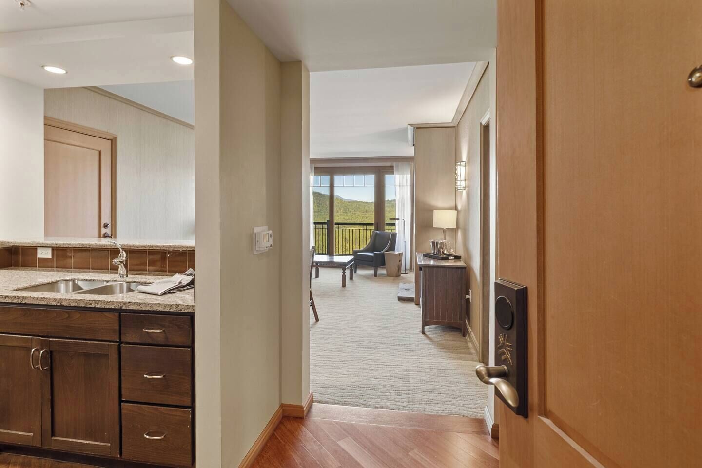 Een hotelkamer met een keukenhoek, een balkon met een stoel en uitzicht op de omgeving.