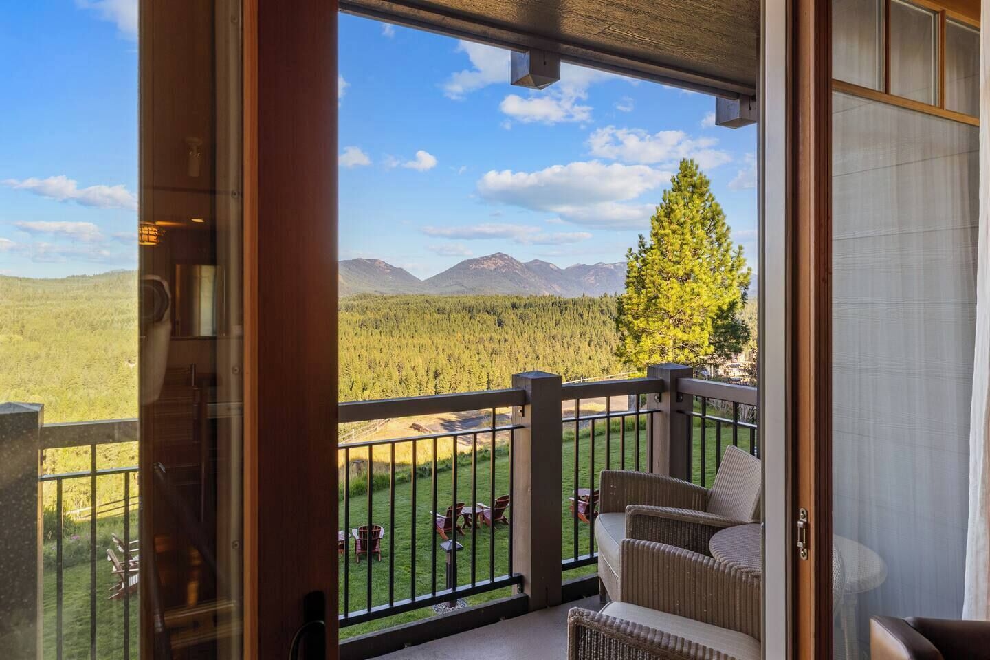 Un balcon offrant une vue sur une forêt et des montagnes, aménagé avec des fauteuils et une table en osier.