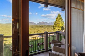 Un balcon offrant une vue sur une forêt et des montagnes, aménagé avec des fauteuils et une table en osier.
