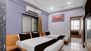 Habitación de hotel con dos camas, un equipo de aire acondicionado, una ventana con cortinas, un cuadro en la pared y una puerta que da a otra habitación.