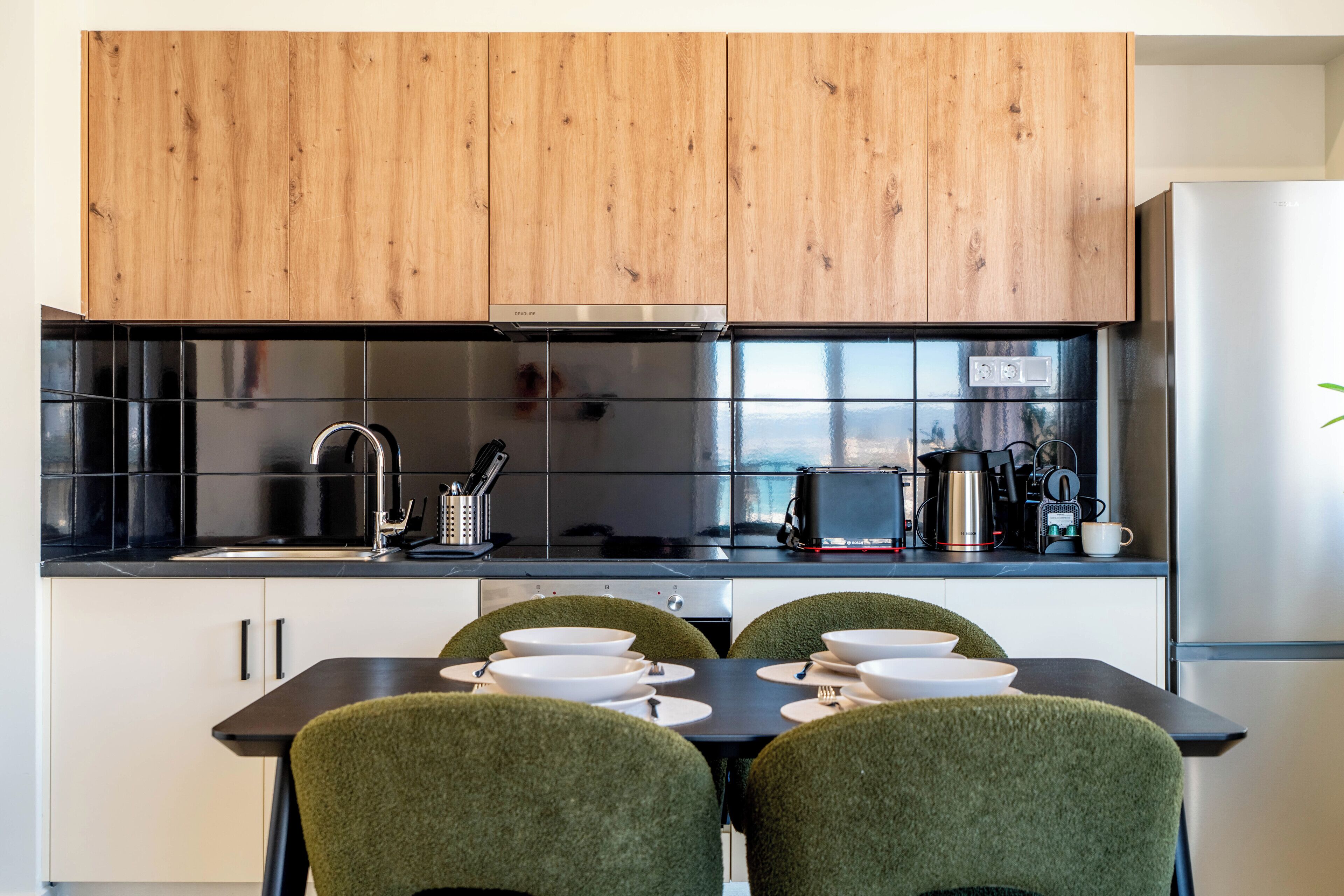 A modern kitchen with wooden cabinets, a black countertop, and a dining table with chairs.