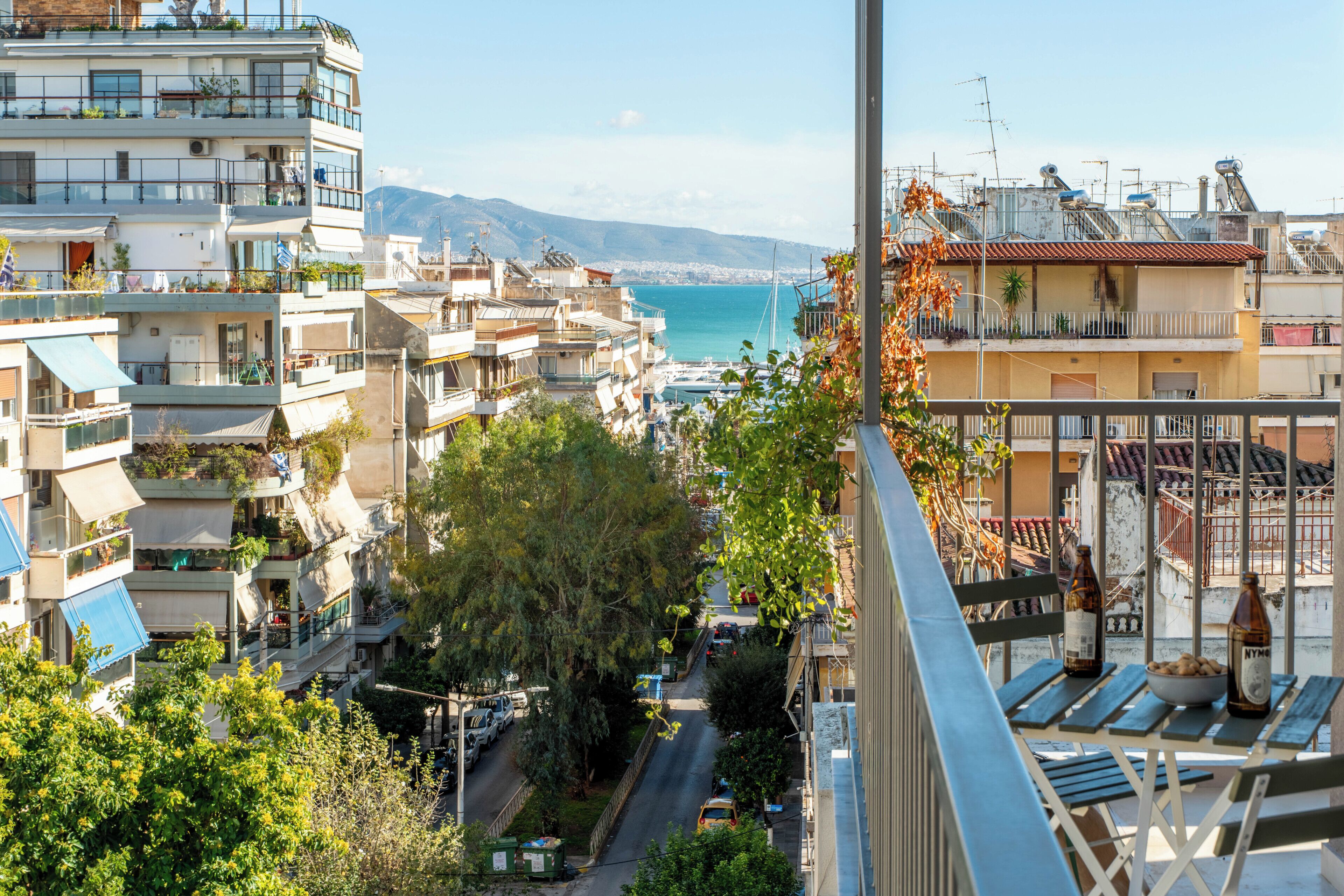 A residential area with multiple-story buildings, a street with parked cars, and a view of the sea in the background.