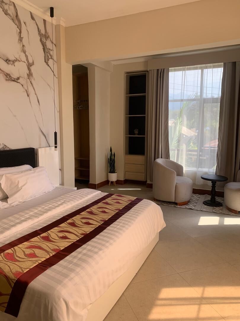 Hotelkamer met een groot bed, een zithoek met twee stoelen, een kleine tafel en uitzicht op het omliggende landschap door een raam.