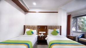 A hotel room with two beds, a wooden headboard, a bedside table with a phone, and a window with curtains. - Treebo Trend Ambassador (Ahmedabad)