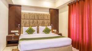 A hotel room with a large bed, two bedside tables, a nightstand, a red curtain, and a wall with a textured design. - Treebo Trend Ambassador (Ahmedabad)