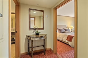 A hotel room with a bed, a bedside table with a plant, a mirror, and a red carpet.