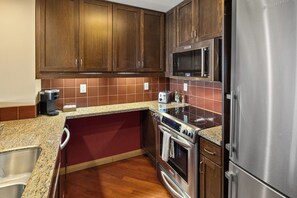 A kitchen with wooden cabinets, a stainless steel refrigerator, a microwave, and a stove.