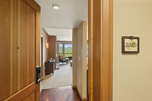 A hotel corridor with wooden doors, a sign indicating room number 2045, and a view of a dining area with a table and chairs.