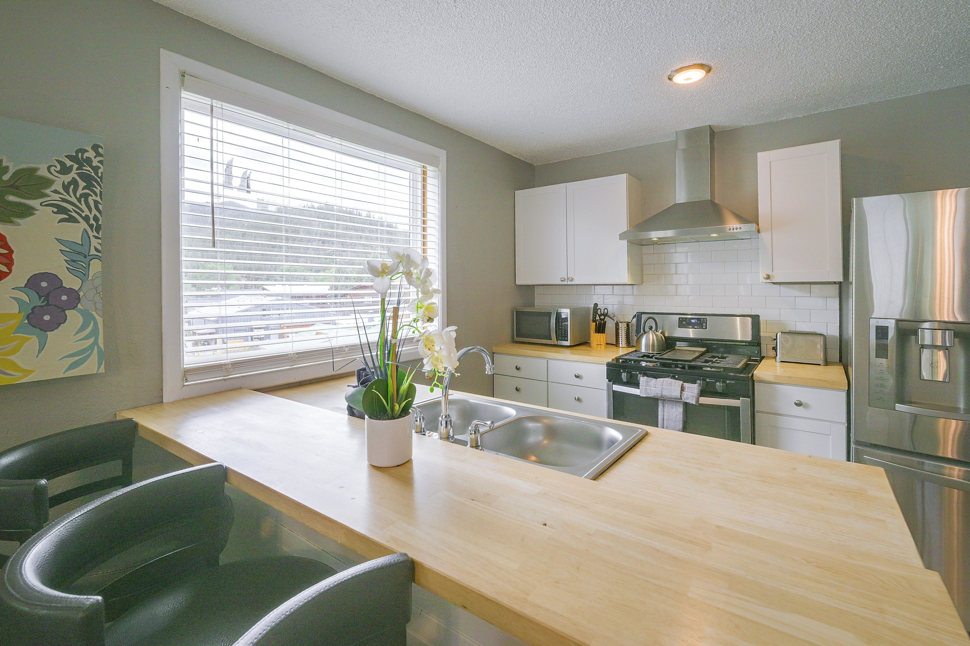 A modern kitchen with a central island, stainless steel appliances, and a window with blinds.