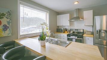 A modern kitchen with a central island, stainless steel appliances, and a window with blinds.