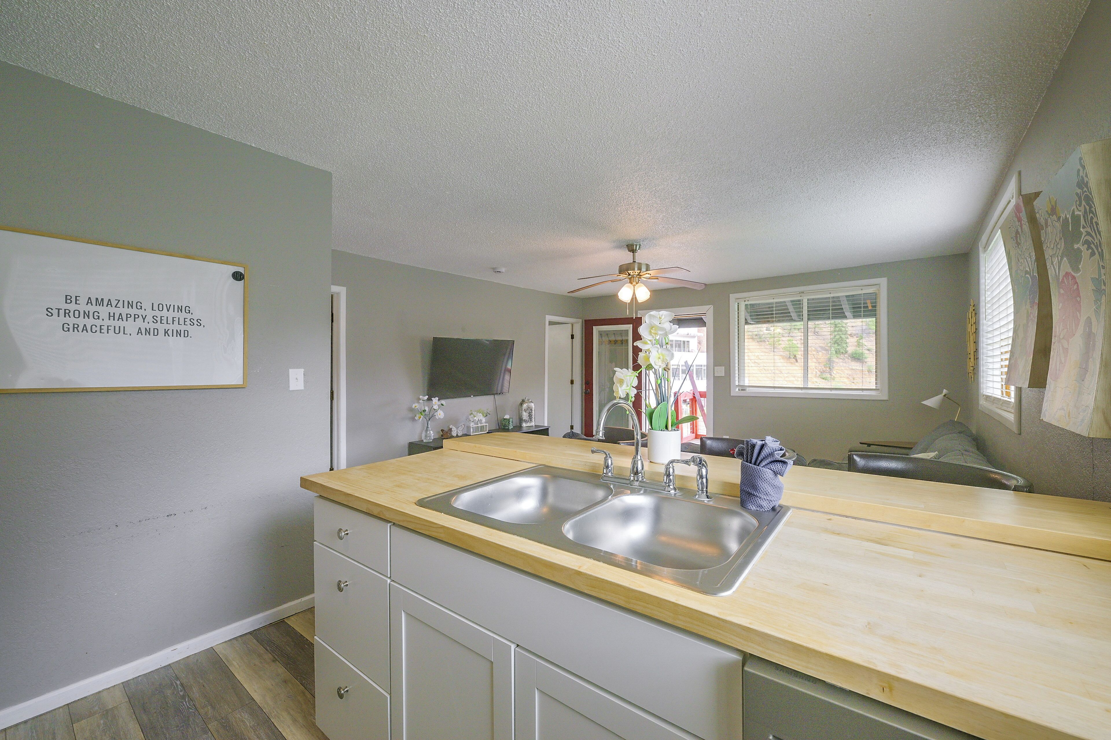 A kitchen with a double sink, wooden countertop, and a ceiling fan.