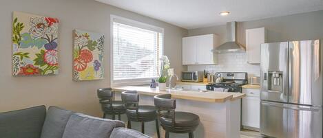 A modern kitchen with a central island, stainless steel appliances, and a seating area with a grey sofa.