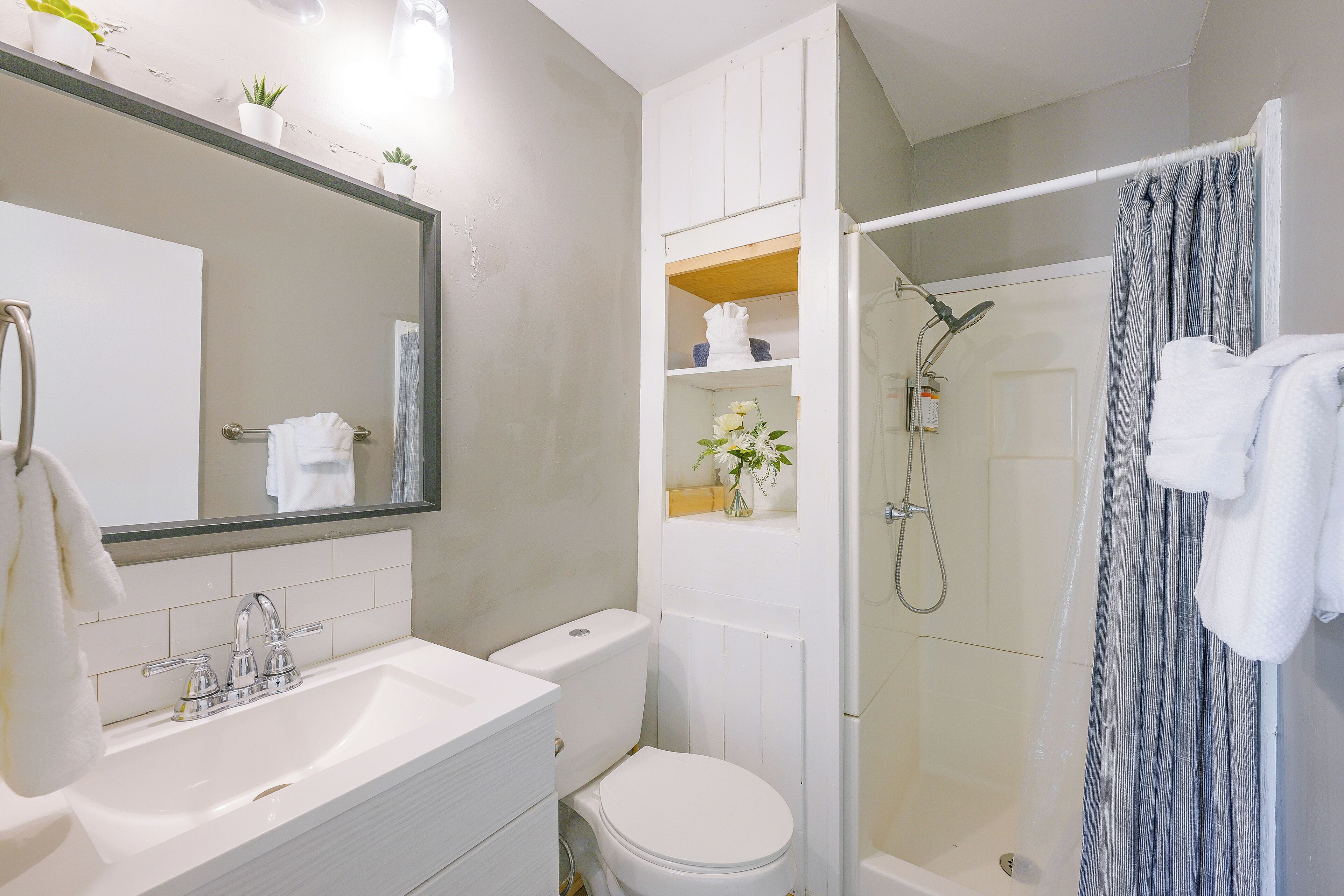 Een badkamer met een wit wastafelmeubel, spiegel, toilet, douche en handdoekhouder.