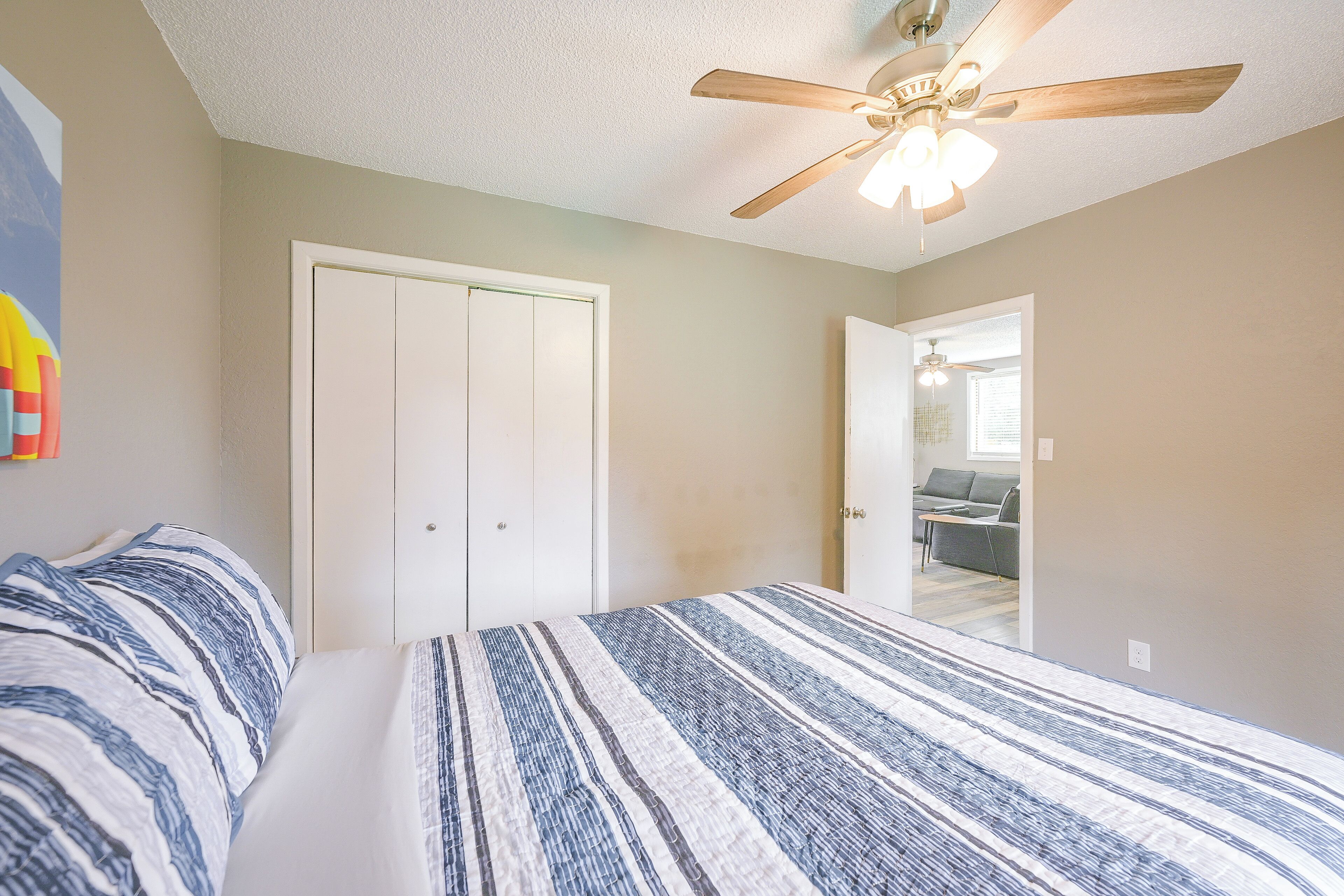 A bedroom with a bed, a ceiling fan, and a door leading to another room.